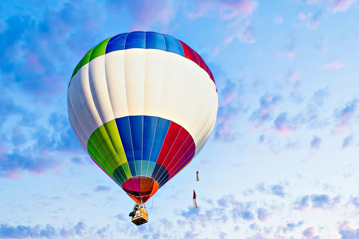 Colorful hot air balloon flying over blue sky with white clouds